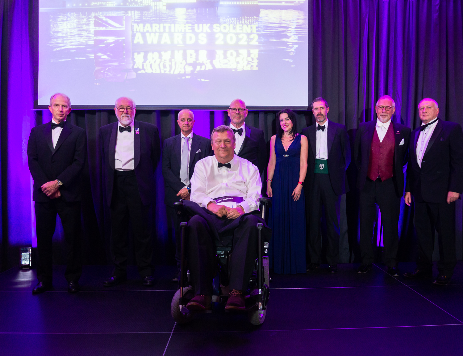 A photo of Maritime UK Solent Awards 2022 Maritime Hero nominees on stage with a purple curtain in the background and a tv screen showing the awards logo image