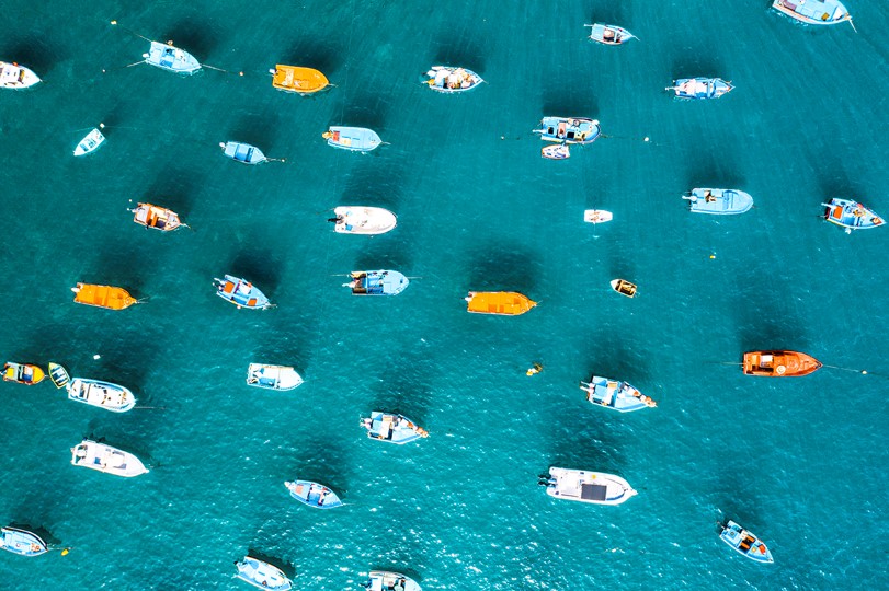 A photo of blue and orange boats from aerial view floating on calm blue waters.
