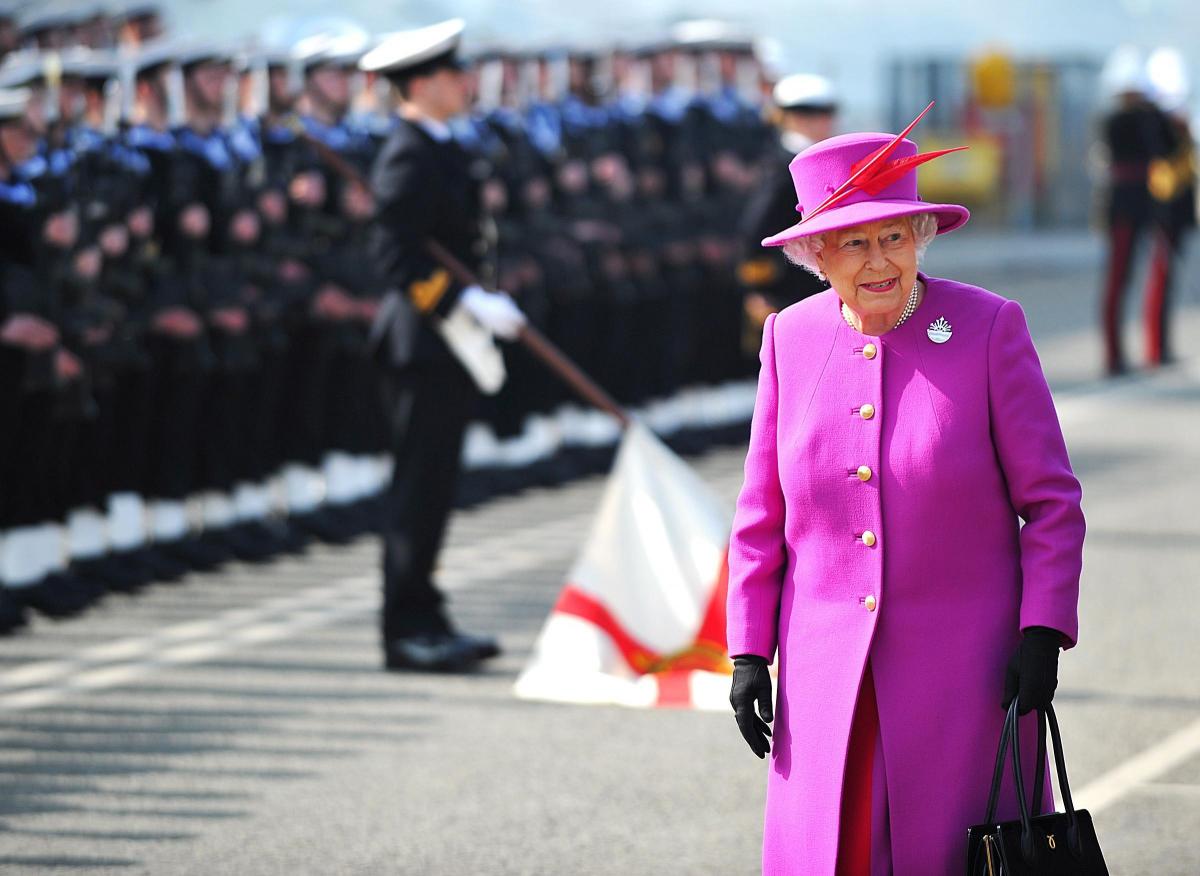 A photo of Her Majesty The Queen at a Portsmouth visit in front of Royal Navy cadets; The Queen is wearing a bright pink coat and hat.