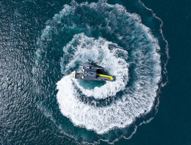 A drone photo of a vessel creating ripples and waves in a circular motion